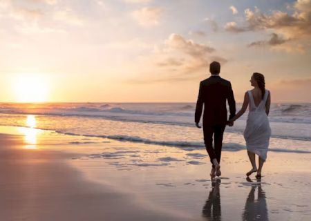 A couple walks hand in hand along a beach at sunset, creating a romantic and serene scene by the ocean with gentle waves and a glowing sky.